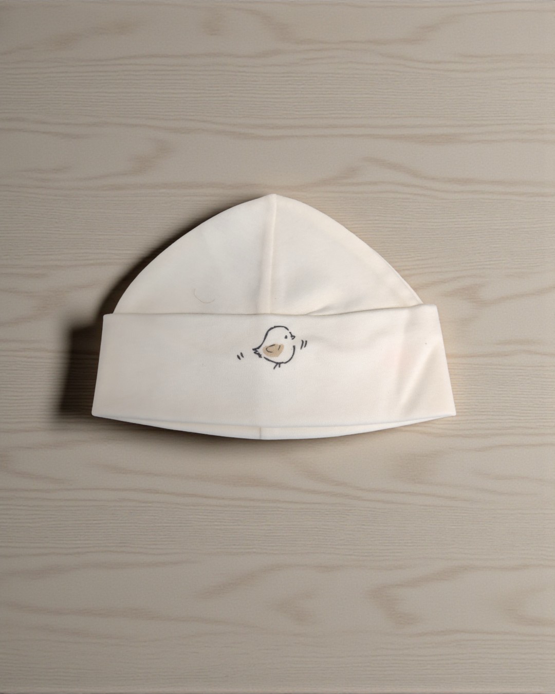 Gorro branco para bebé com desenho de pássaro pequeno.