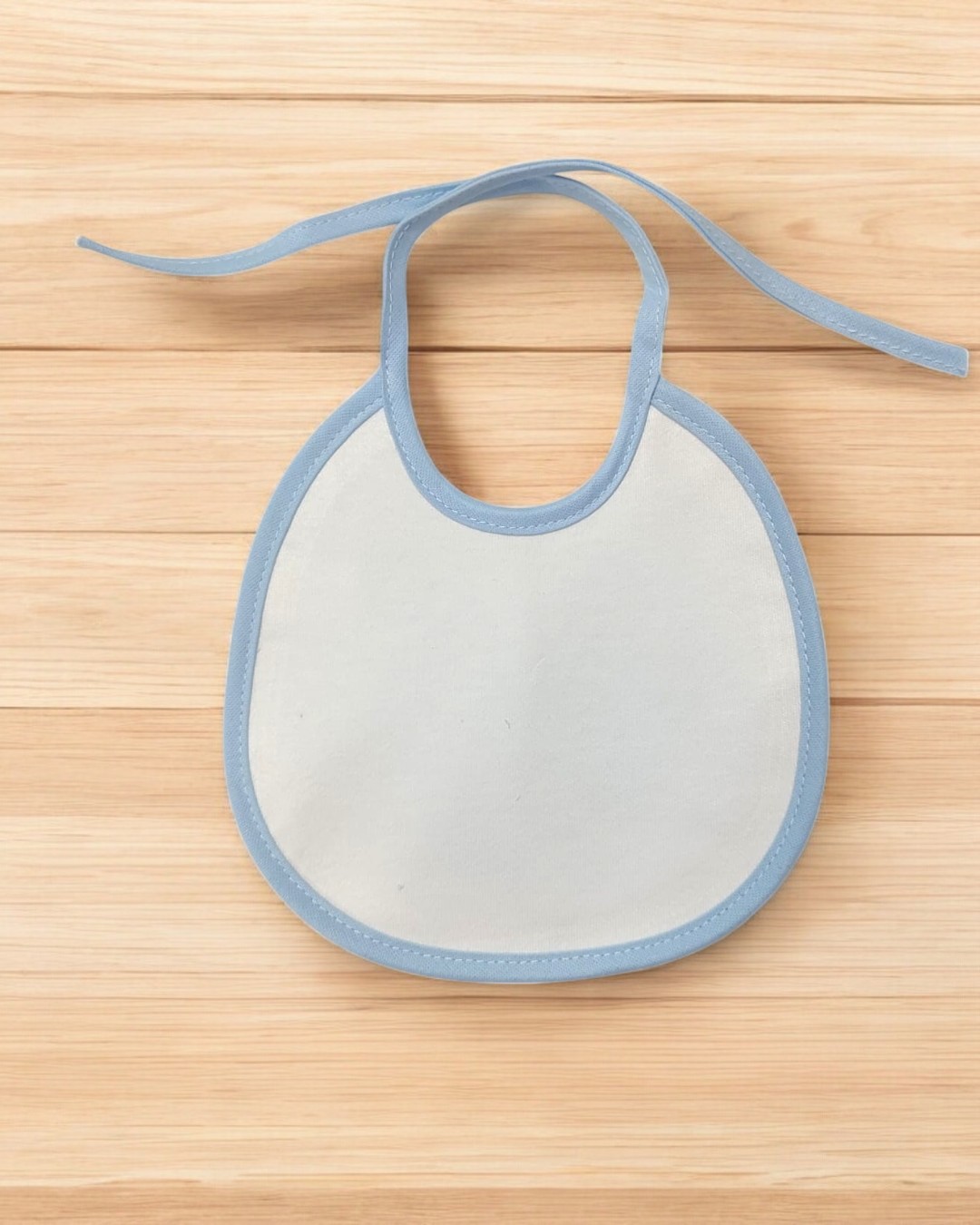 Babete de bebé branco com bordas azuis sobre madeira clara