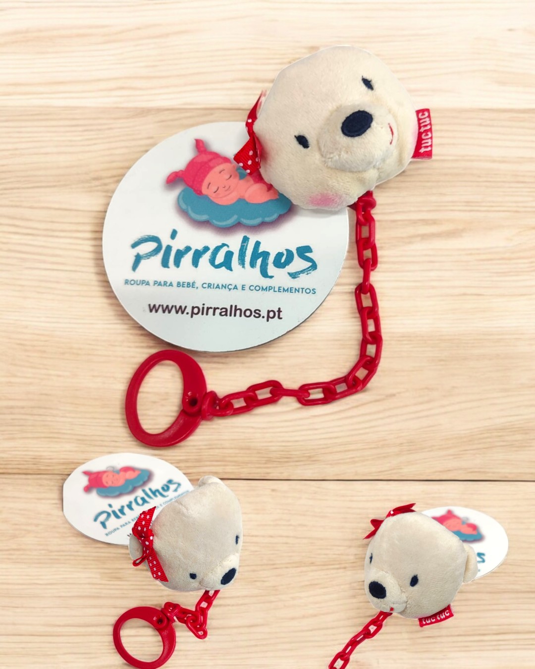 Brinquedo de pelúcia em forma de cabeça de urso com corrente vermelha e etiqueta da marca Pirralhos