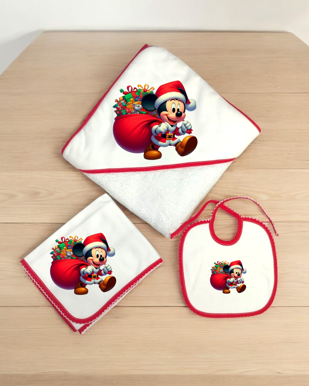 Conjunto de toalha, fralda e babete brancos com bordas vermelhas e imagem do Mickey Mouse vestido de Pai Natal.