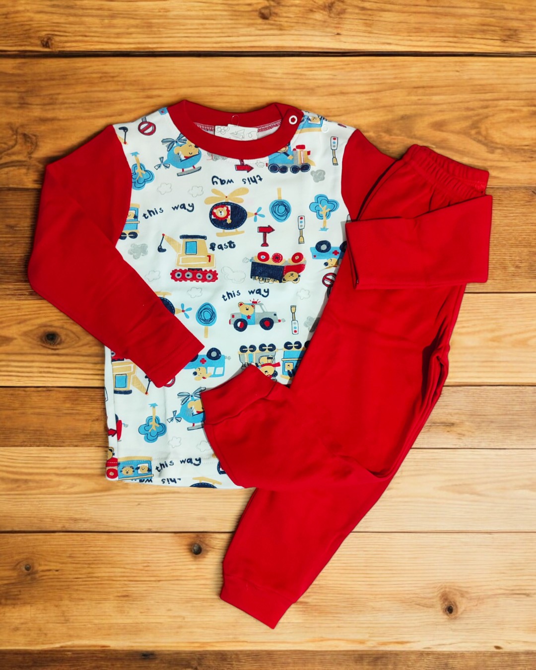 Pijama de criança com camisola estampada e calças vermelhas sobre piso de madeira.