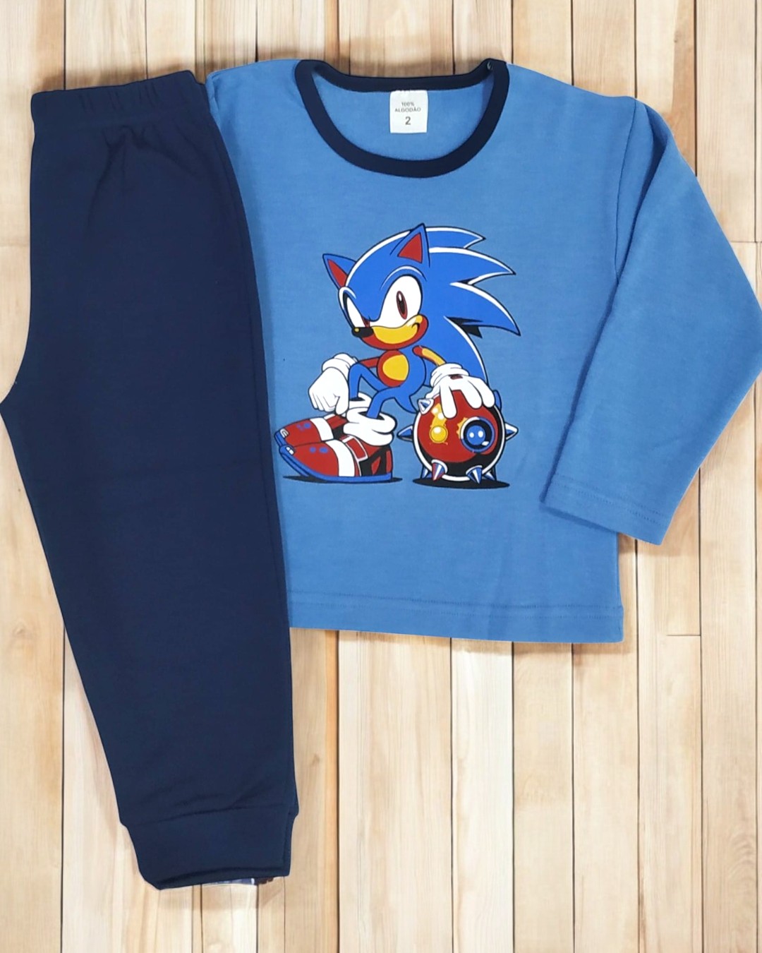 Pijama infantil azul com personagem Sonic e calças azul escuro sobre chão de madeira.