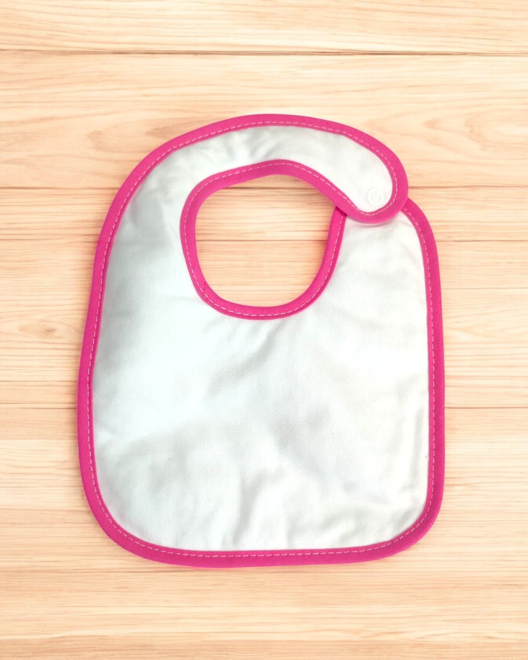 Babete para bebé branco com borda rosa em superfície de madeira
