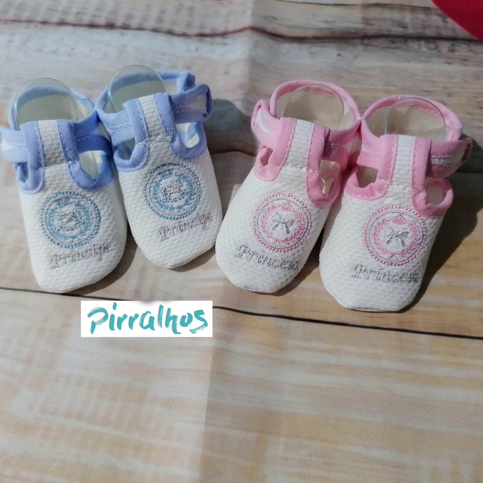 Dois pares de sapatinhos de bebê, azul e rosa, com bordado e palavra Pirralhos
