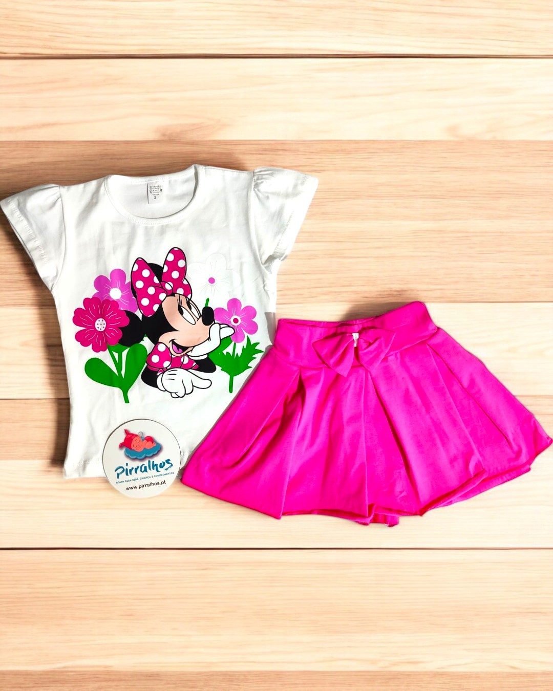 Conjunto infantil Minnie Mouse com t-shirt branca e saia rosa sobre madeira clara