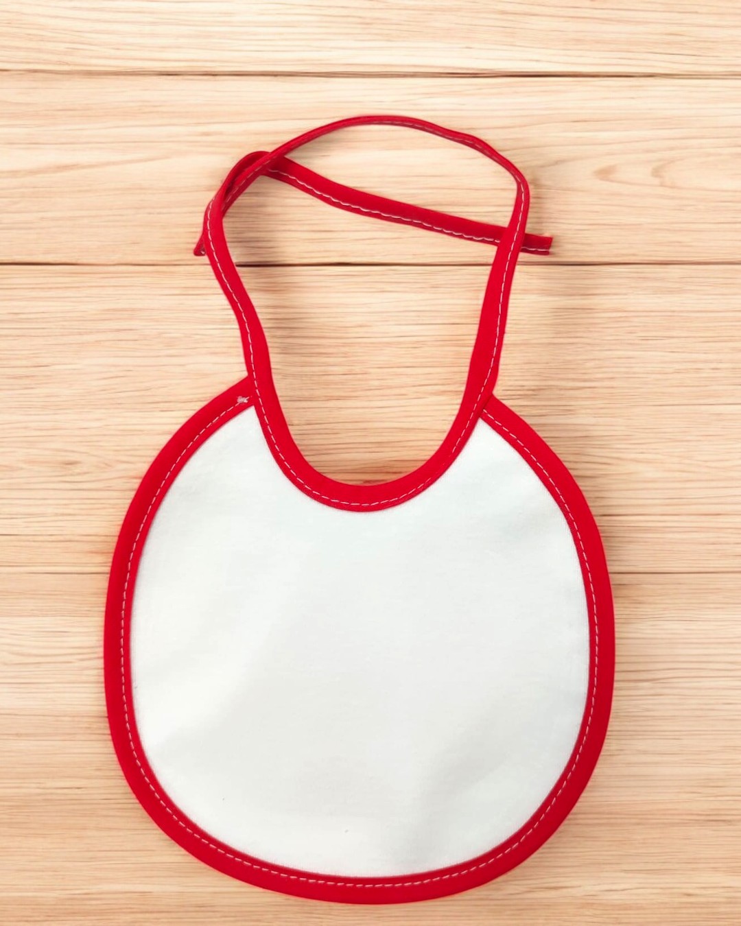 Babete para bebé branco com borda vermelha sobre superfície de madeira clara