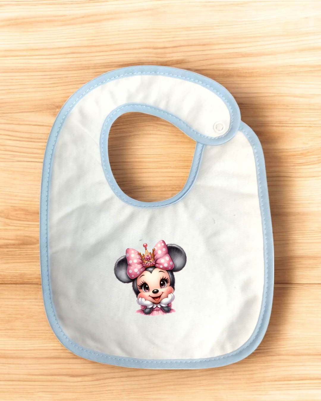 Babete branco com borda azul e estampa de personagem infantil com laço rosa e coroa