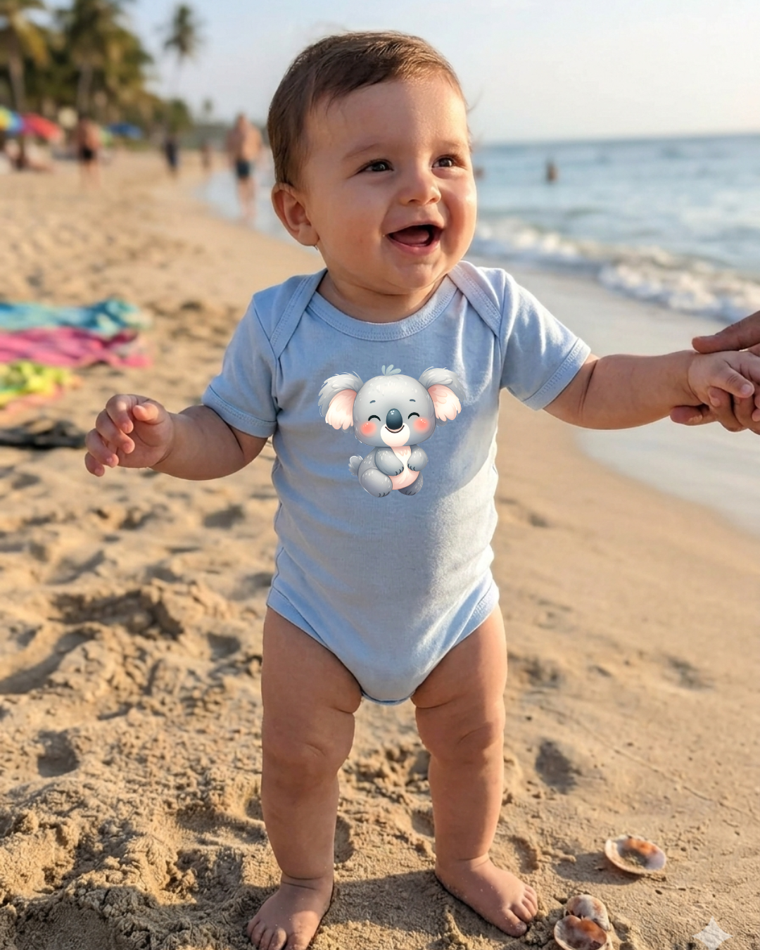 Bebé na praia de body azul com estampa de coala