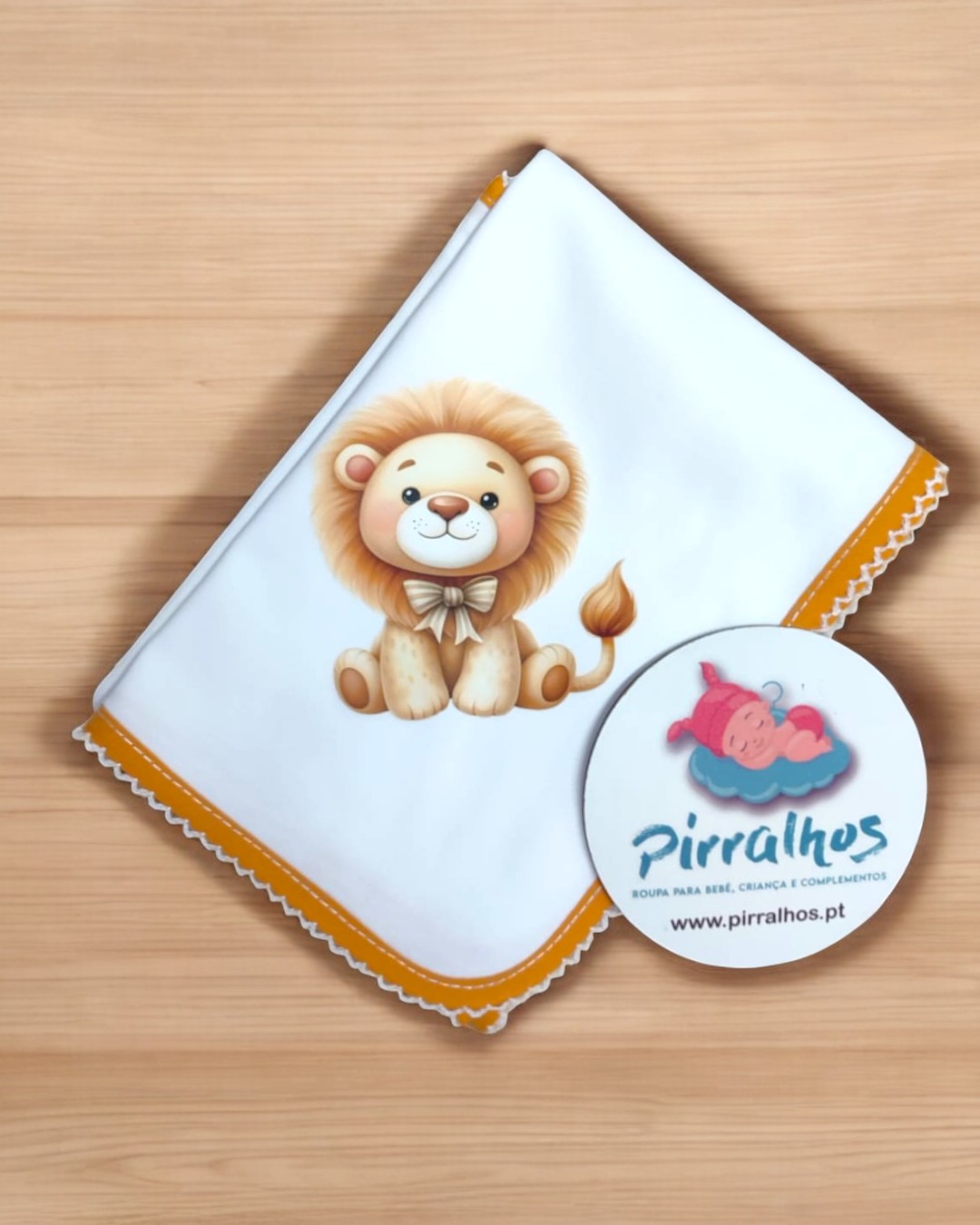 Manta branca com borda amarela e estampa de leão sorridente, etiqueta redonda da marca Pirralhos