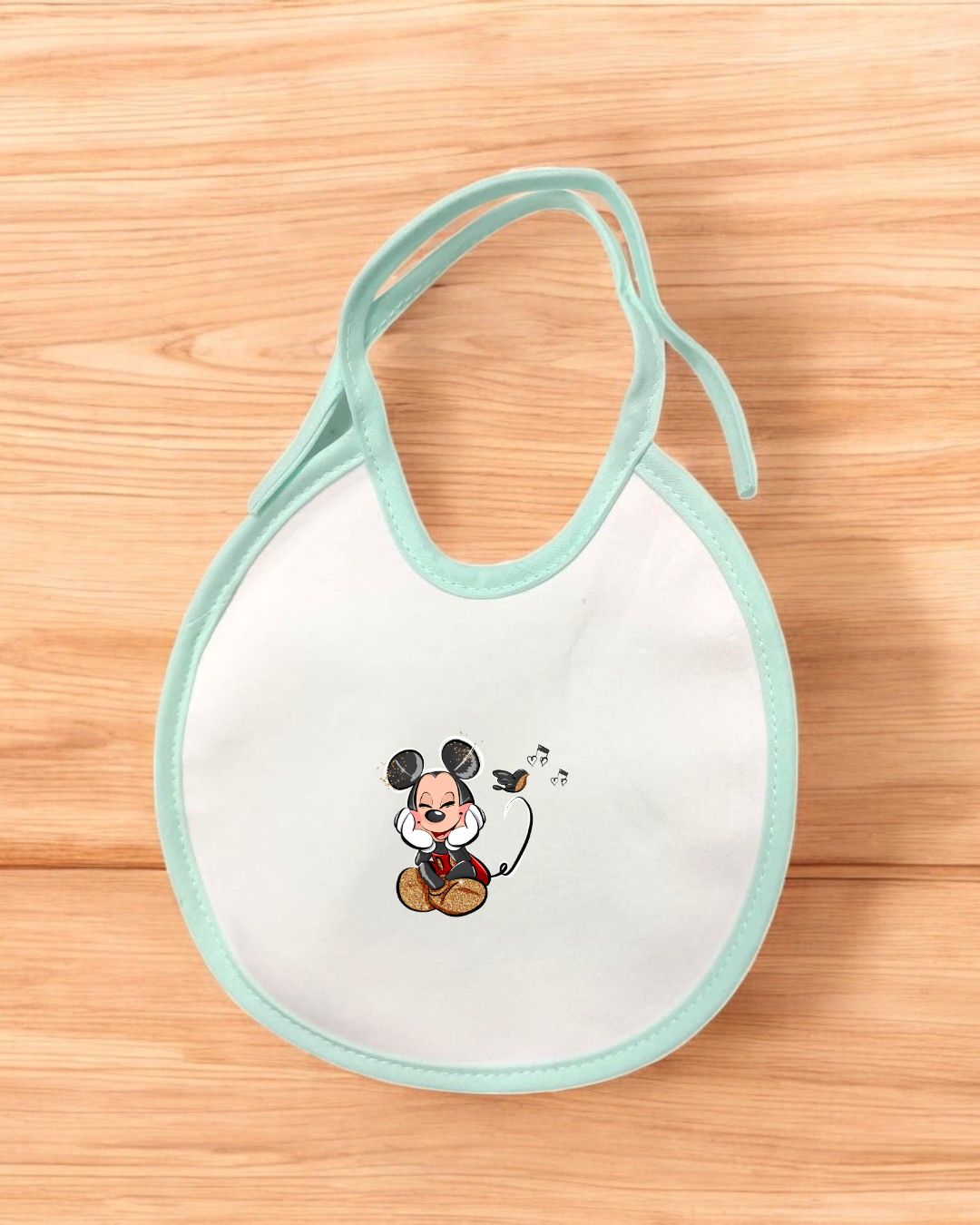 Babete branco com borda azul clara e Mickey Mouse a dançar, num fundo de madeira clara