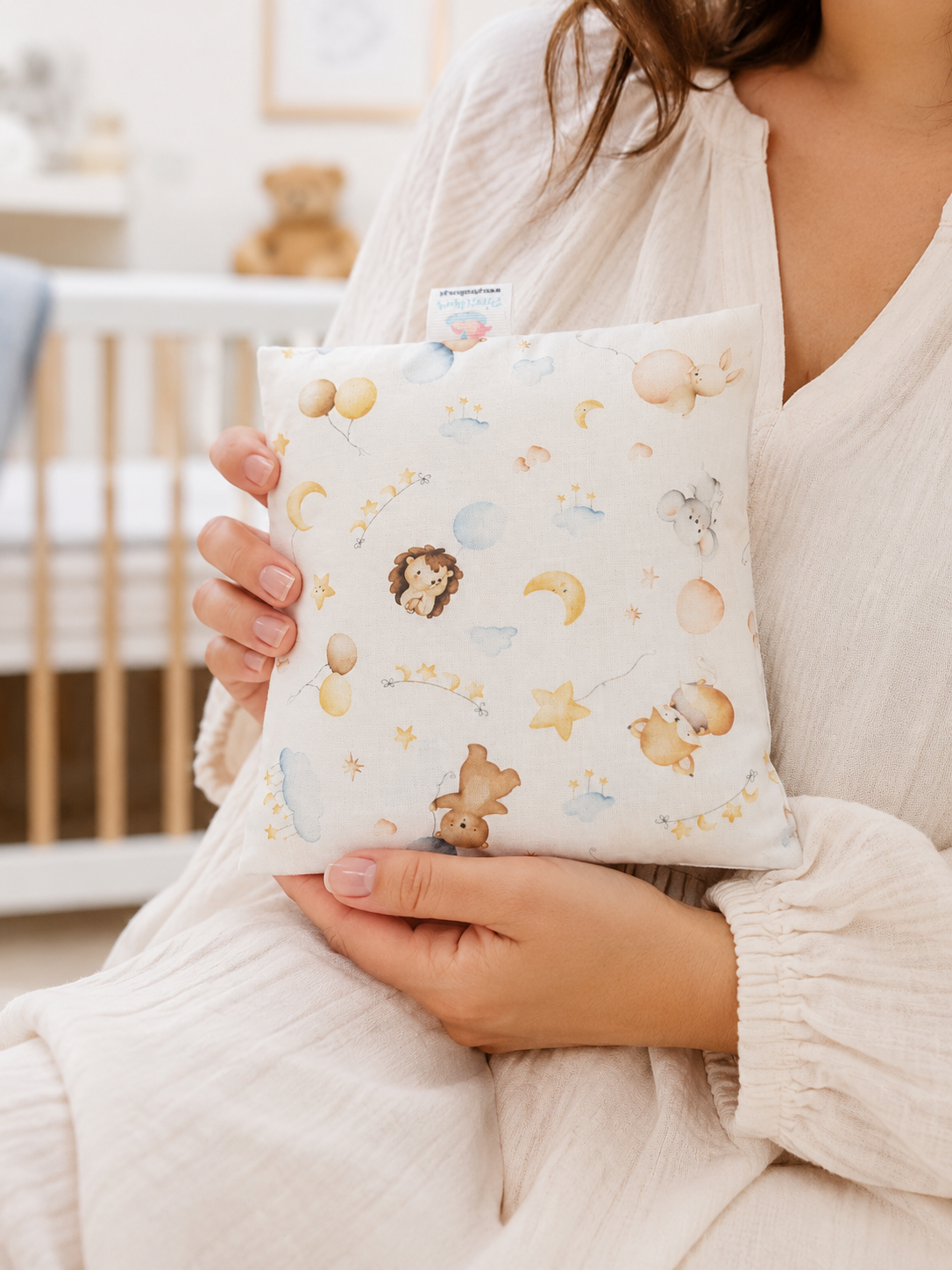 Almofada infantil com estampa de animais e elementos celestiais segura por pessoa em quarto de bebé