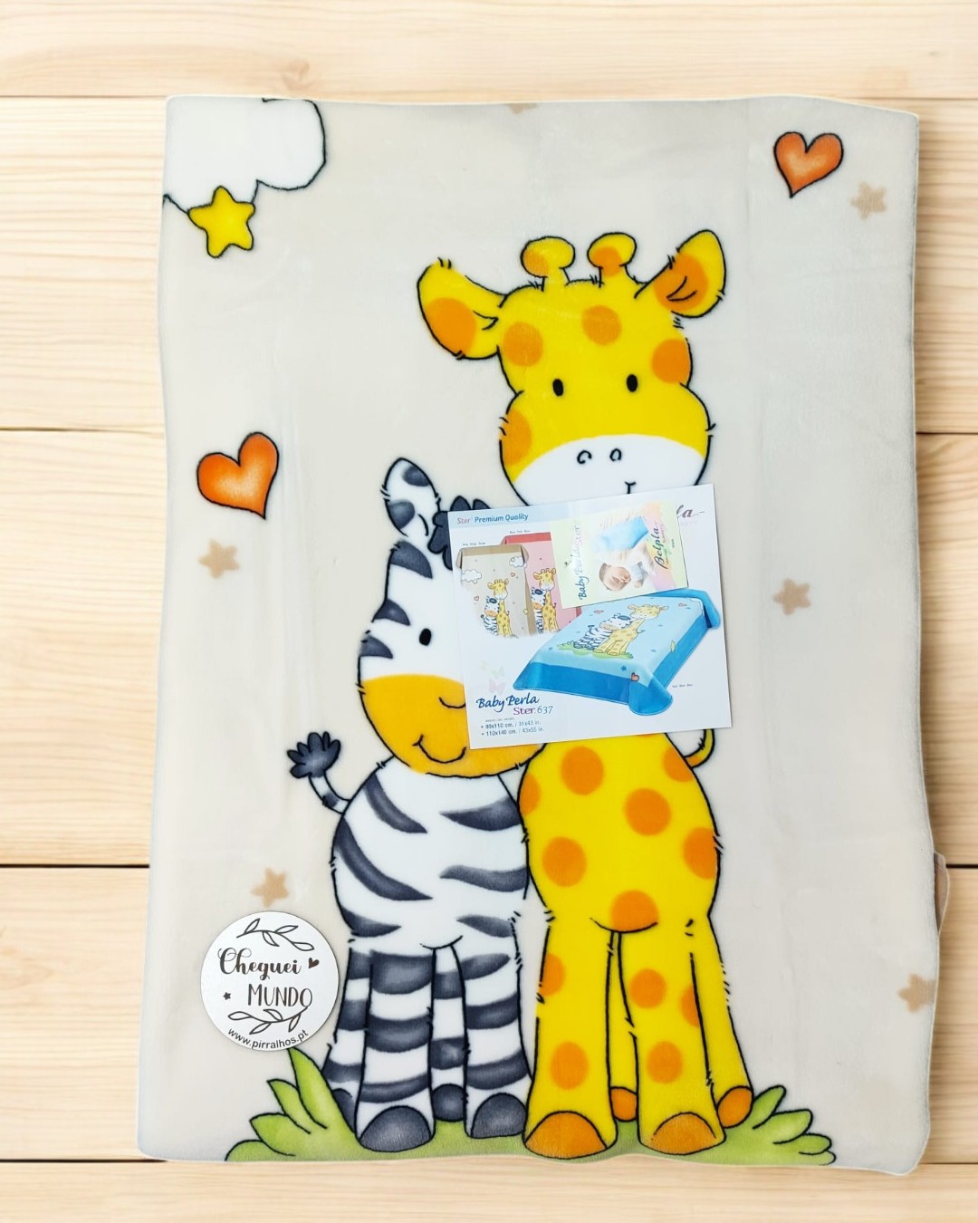 Cobertor com estampa de girafa e zebra coloridos sobre madeira clara.