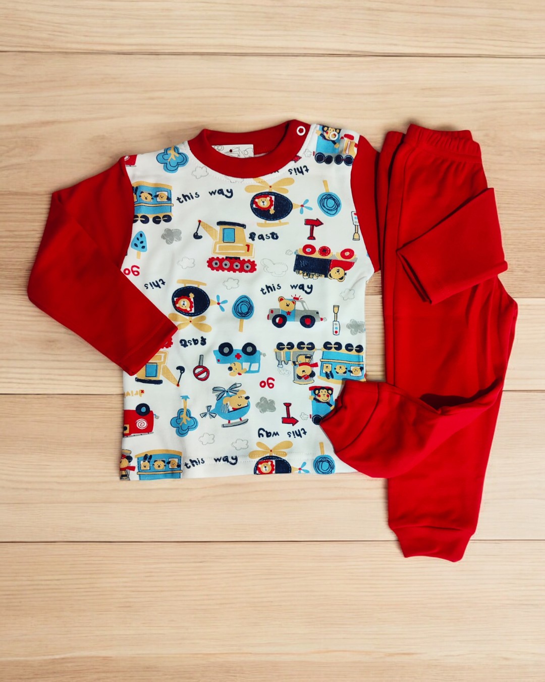 Pijama infantil vermelho com padrão de carrinhos e helicópteros sobre madeira clara