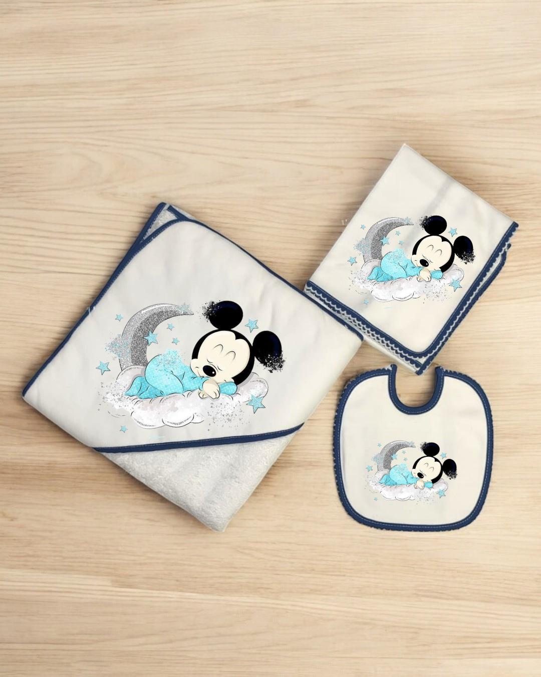 Conjunto de toalha, fralda e babete de bebé com desenho do Mickey Mouse a dormir numa nuvem.