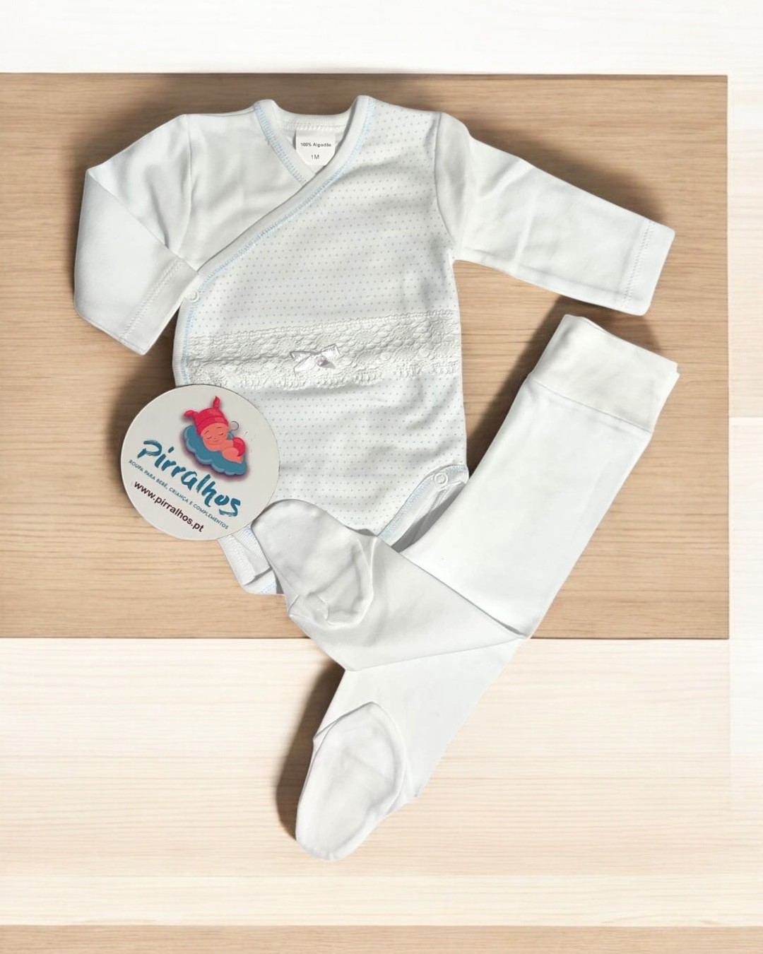 Conjunto de roupa para bebé branca com etiqueta Pirilitos sobre madeira.