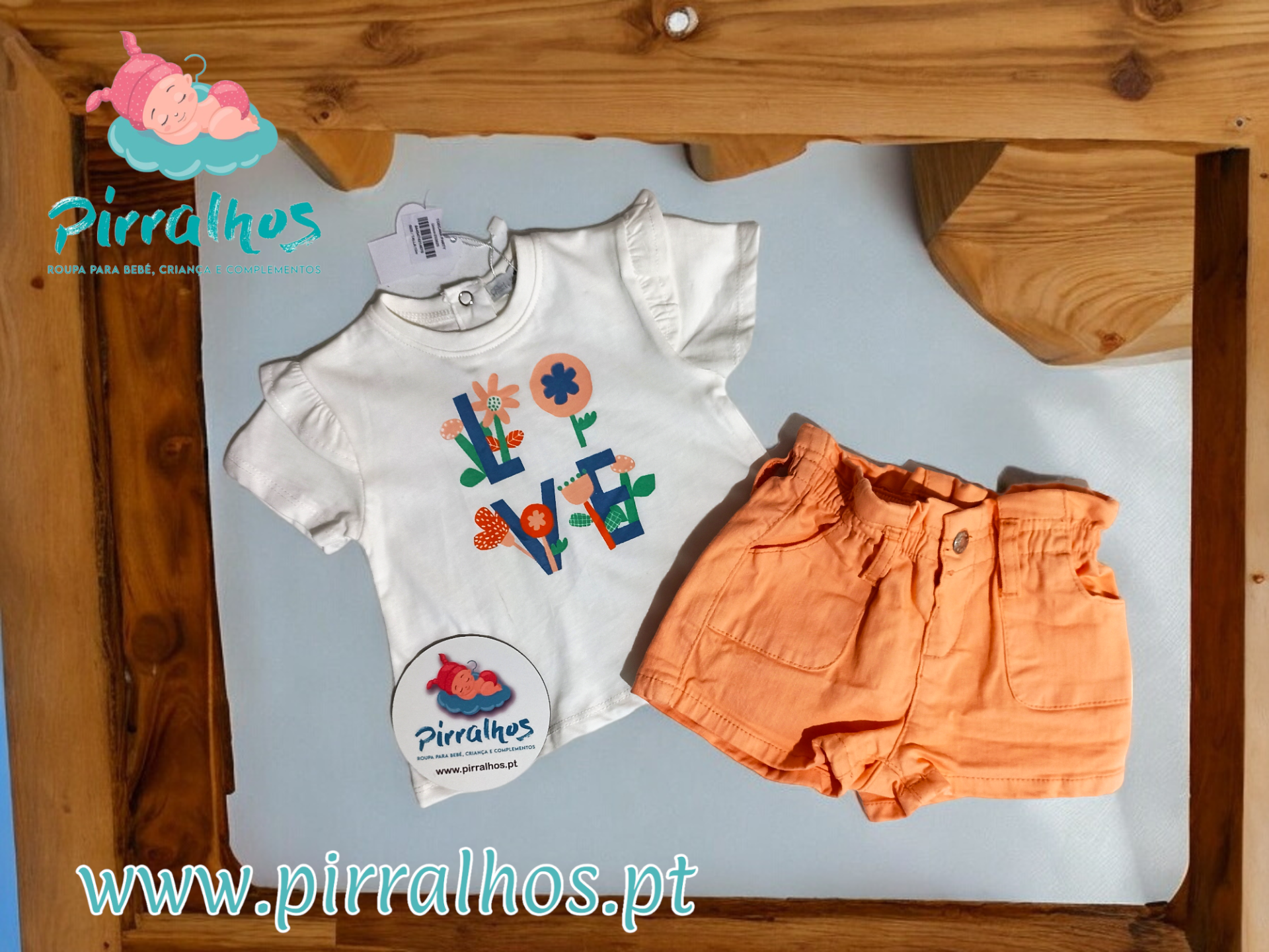 Conjunto de roupa infantil com t-shirt branca e calções laranja sobre fundo branco e moldura de madeira