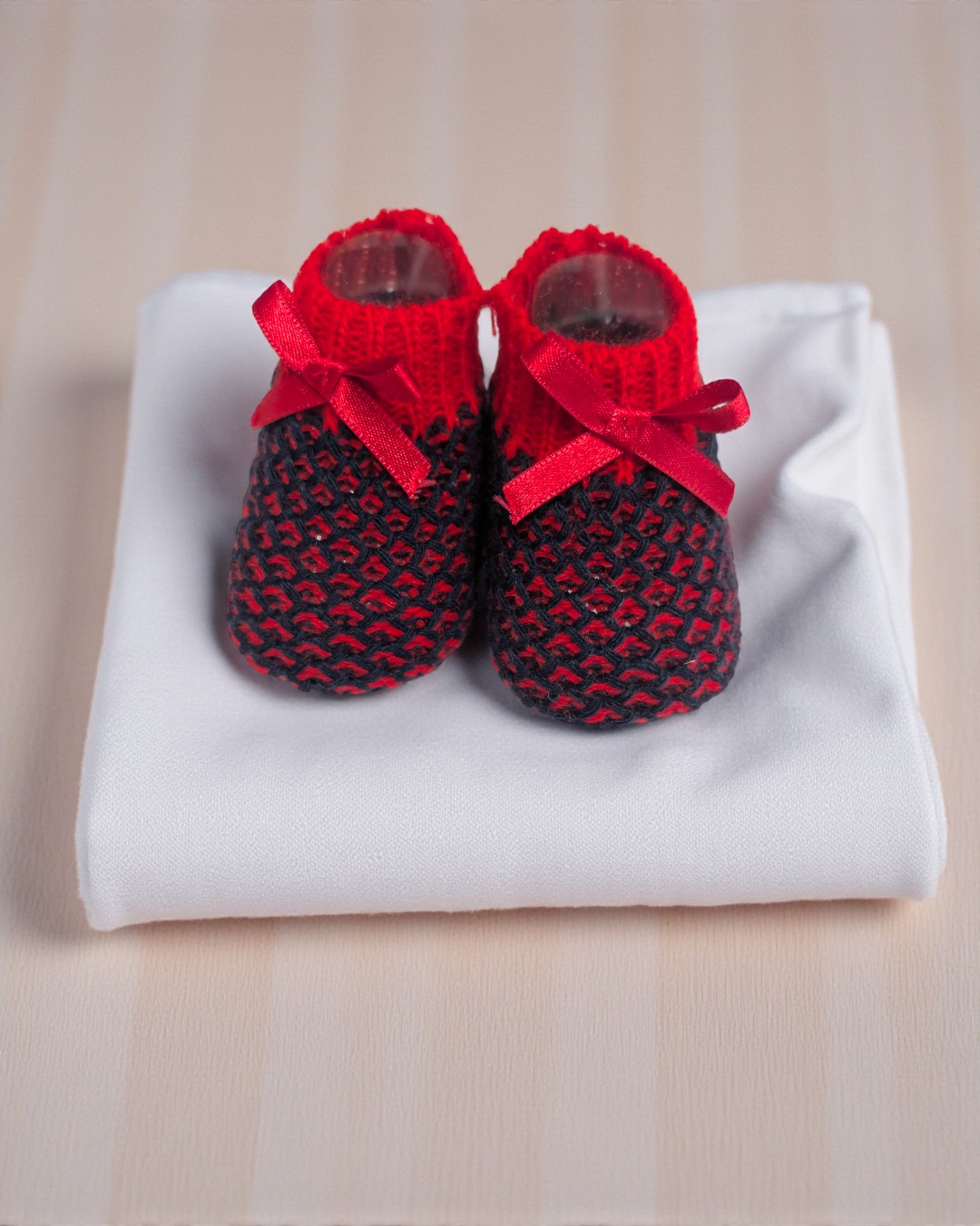 Sapatinhos de bebé vermelhos e pretos com laços vermelhos sobre pano branco