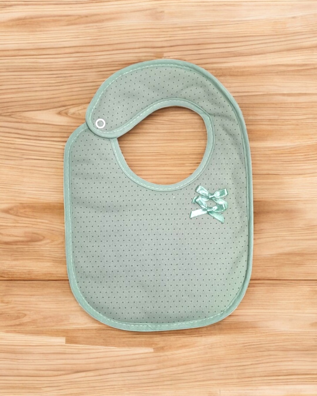 Babeiro verde-água com pontos pequenos e laços, sobre superfície de madeira
