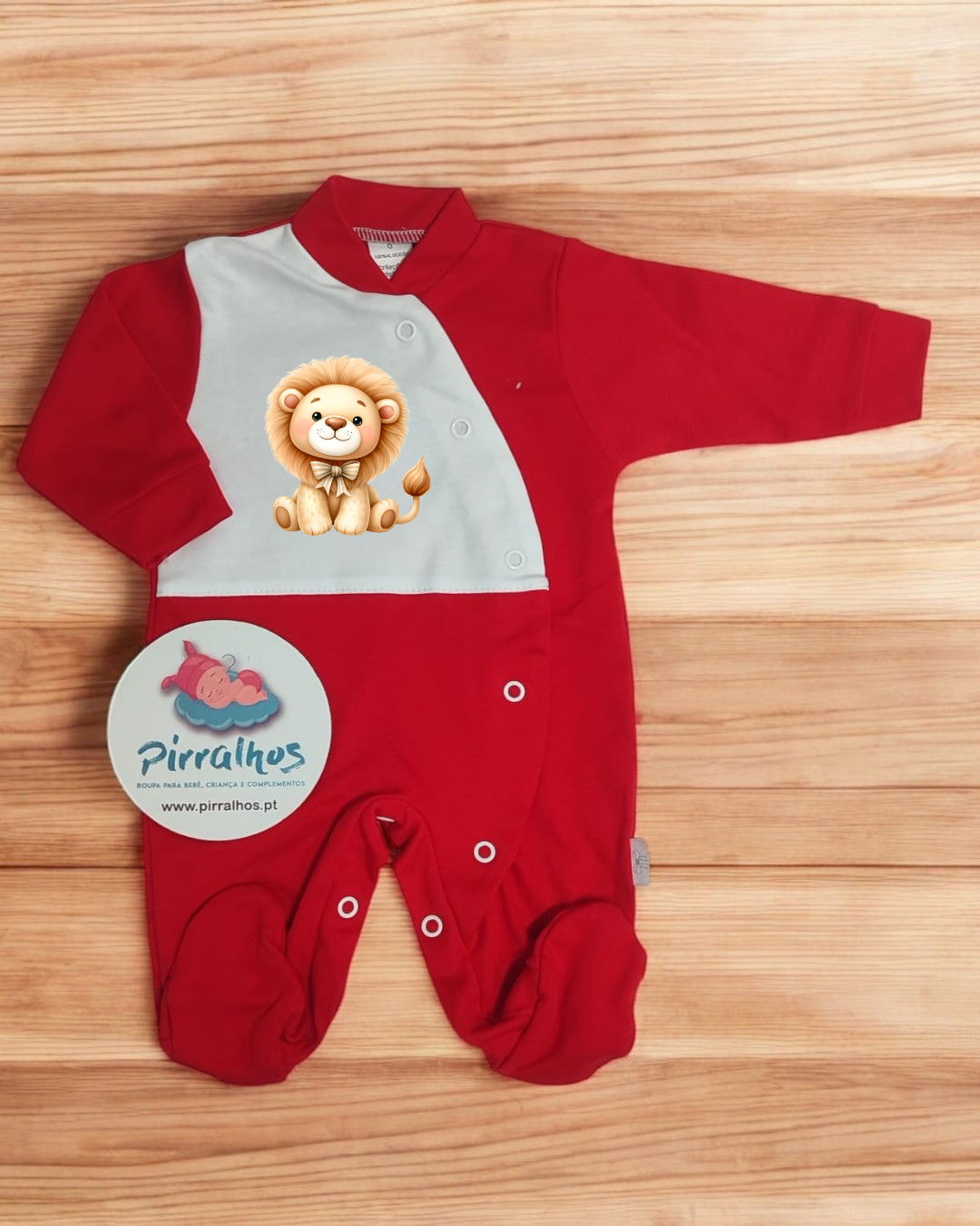 Macacão de bebé vermelho e branco com imagem de leão e etiqueta com texto pirralhos numa superfície de madeira clara.