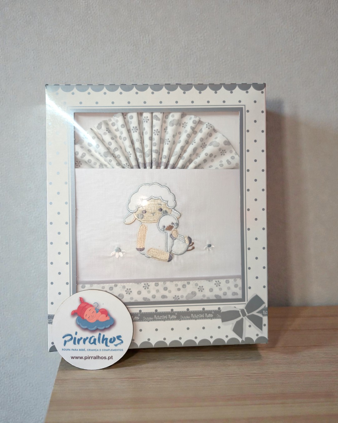 Conjunto de roupas para bebé com bordado de ovelha e pato em embalagem decorada com pontos cinzentos.