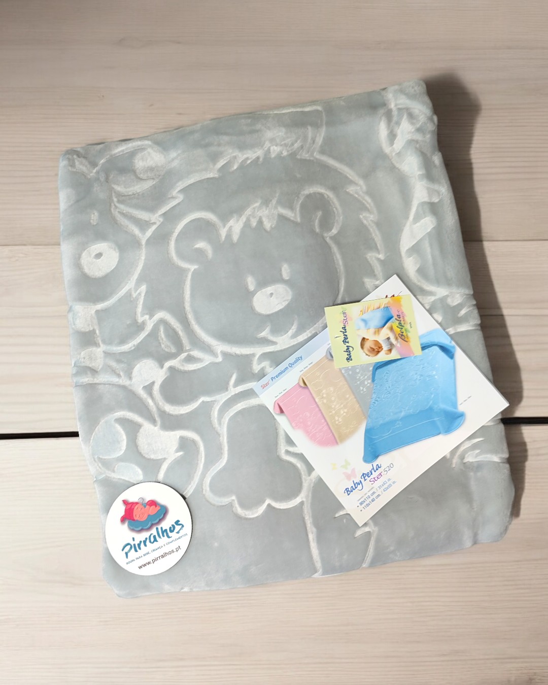 Manta cinzenta com padrão de urso em relevo e etiqueta de marca sobre madeira clara