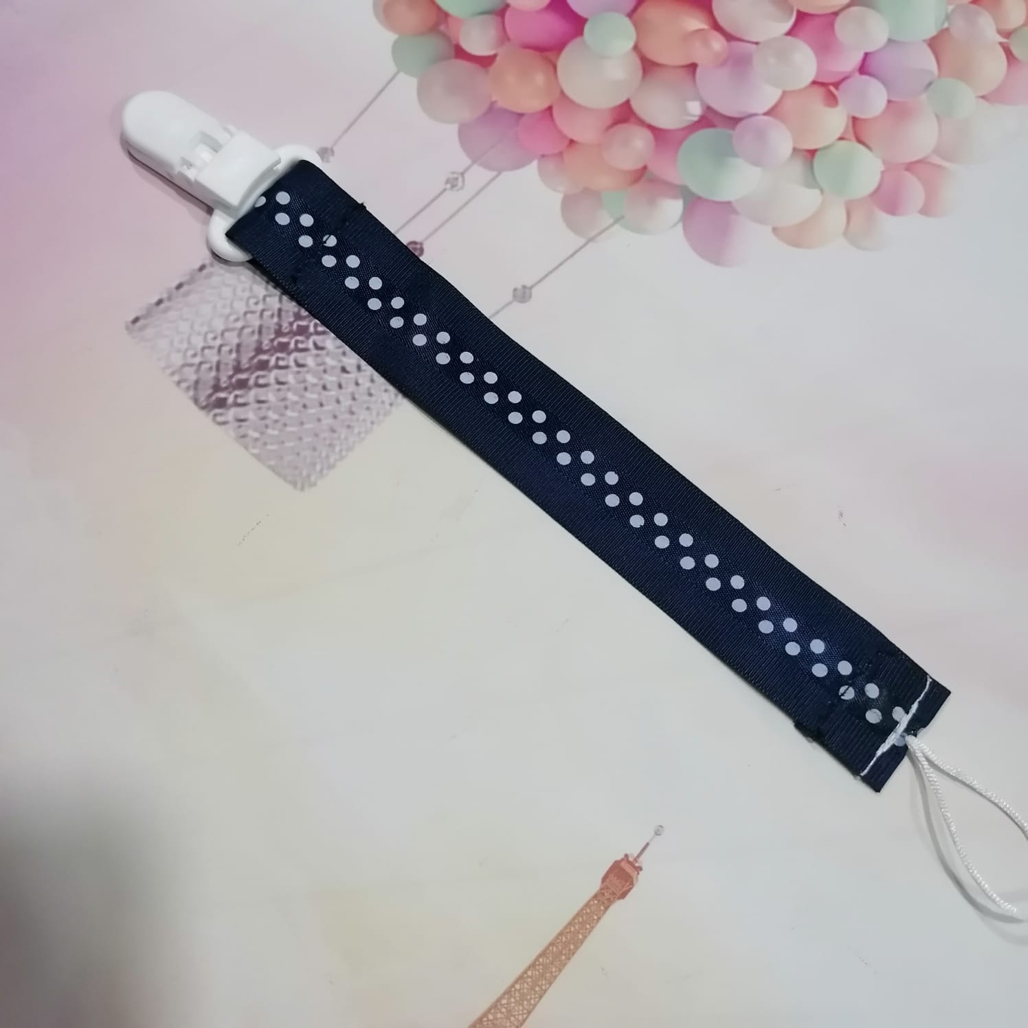 Prendedor de chupeta azul escuro com formas brancas numa superfície com balões coloridos