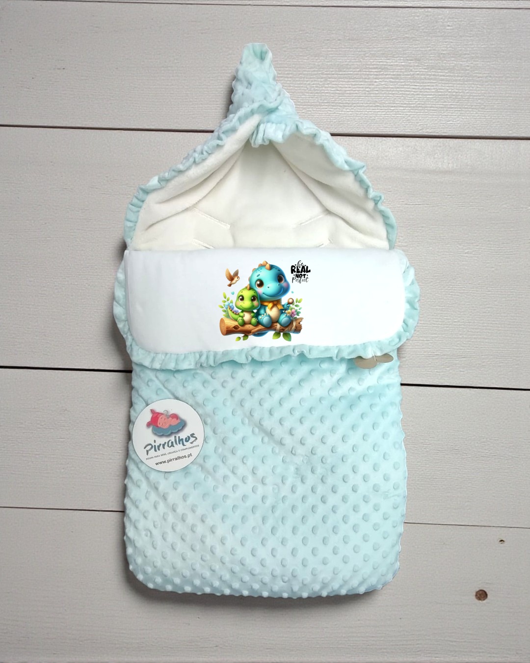 Saco de bebé azul claro com estampa de dinossauros e etiqueta da marca Pirralhos