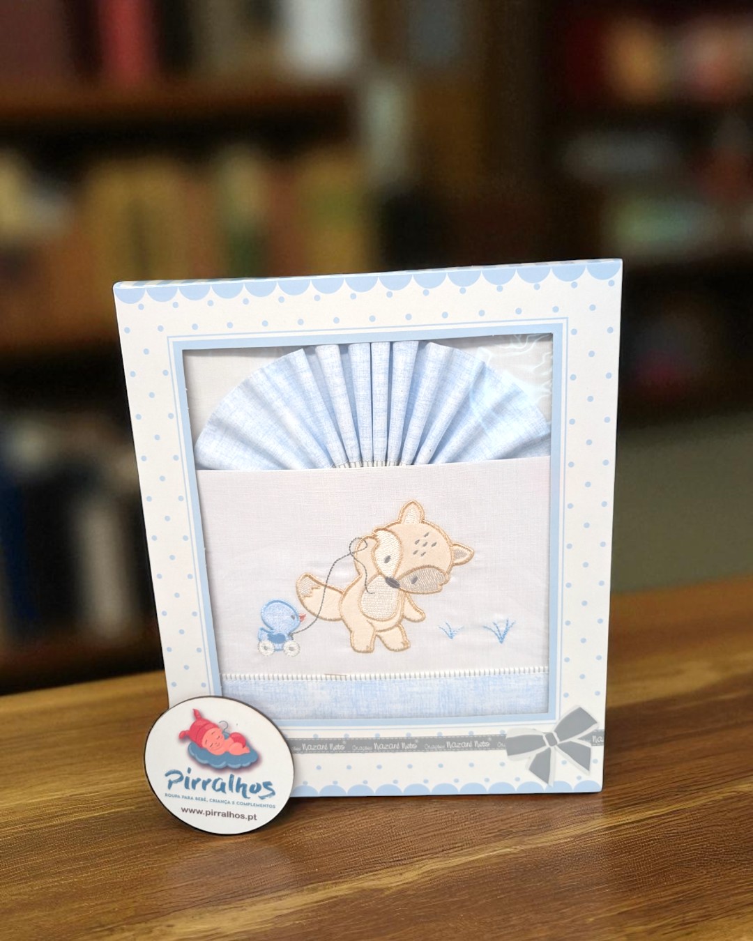 Conjunto para bebé azul claro e branco com bordado de cão numa caixa decorada.