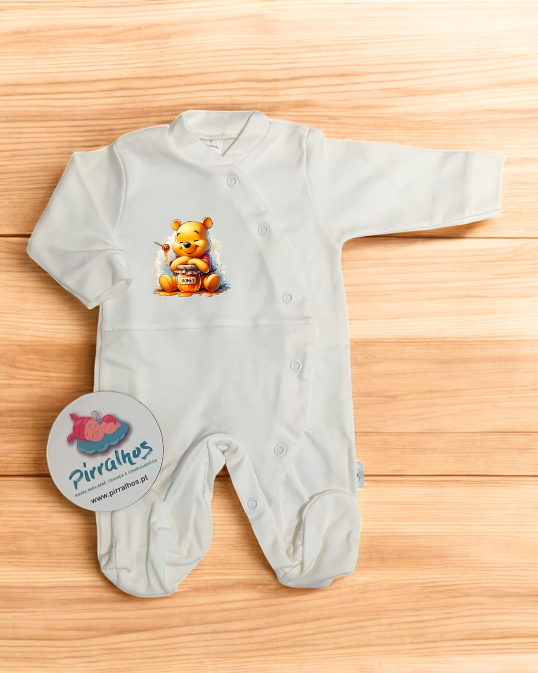 Macacão de bebé branco com estampa de urso e etiqueta redonda.