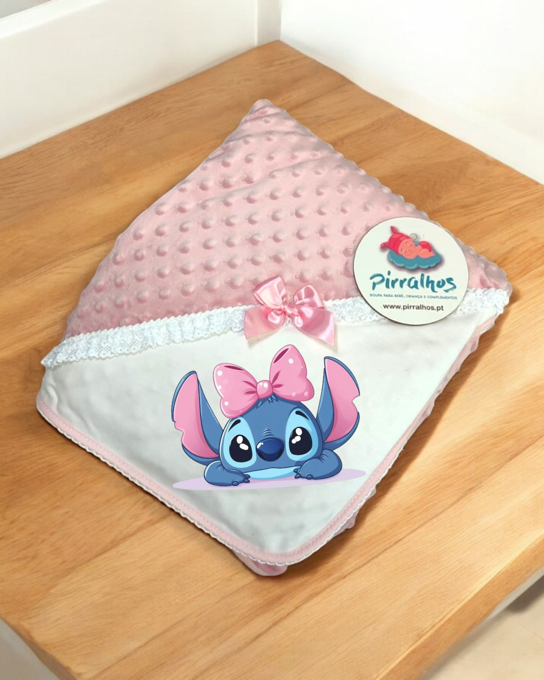 Manta rosa para bebé com personagem Stitch e laço cor de rosa numa superfície de madeira