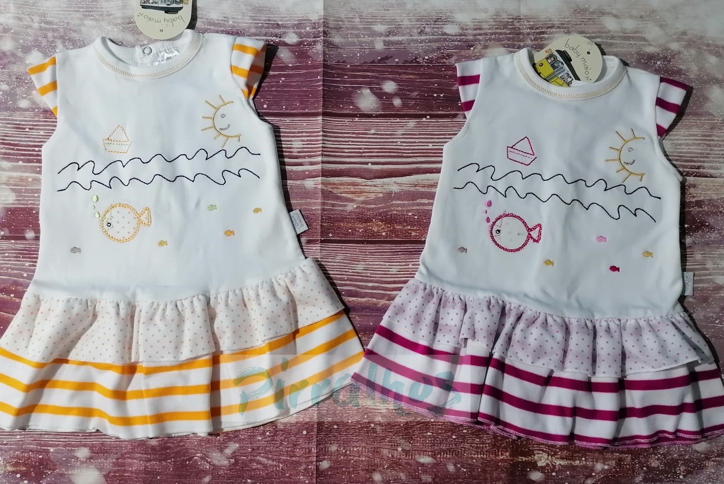 Dois vestidos infantis brancos com estampas e saias riscas amarelo e rosa sobre fundo de madeira