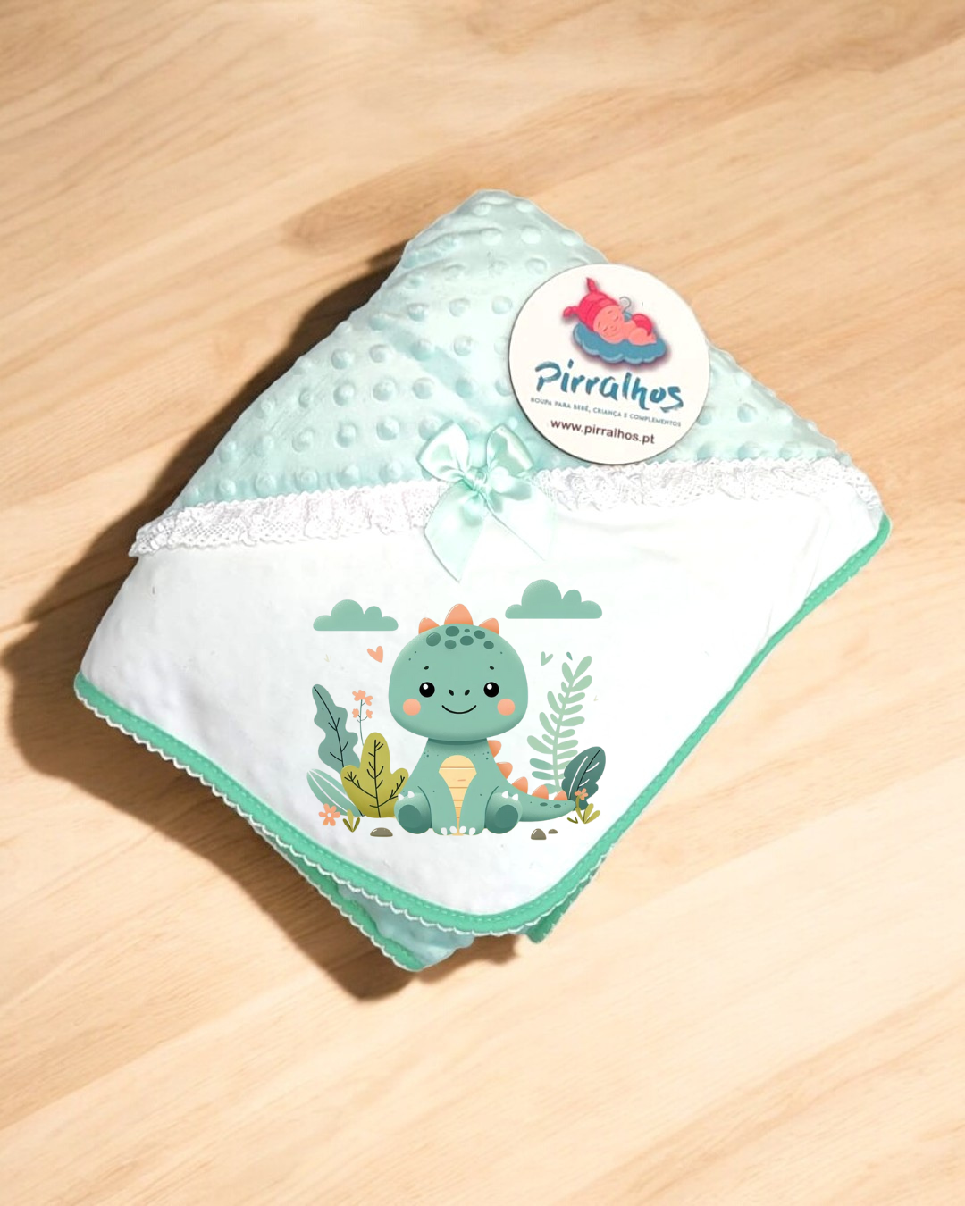Manta infantil verde com desenho de dinossauro e etiqueta da marca Pirralhos