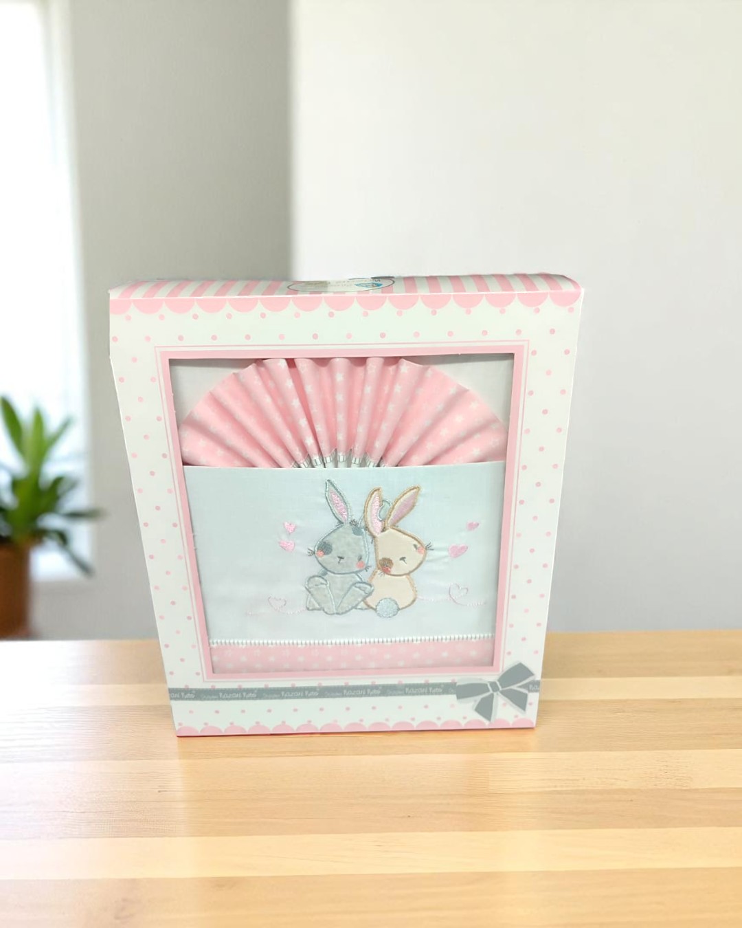 Jogo de roupa de cama para bebé com padrão rosa e ilustração de dois coelhos embrulhado numa caixa branca e rosa