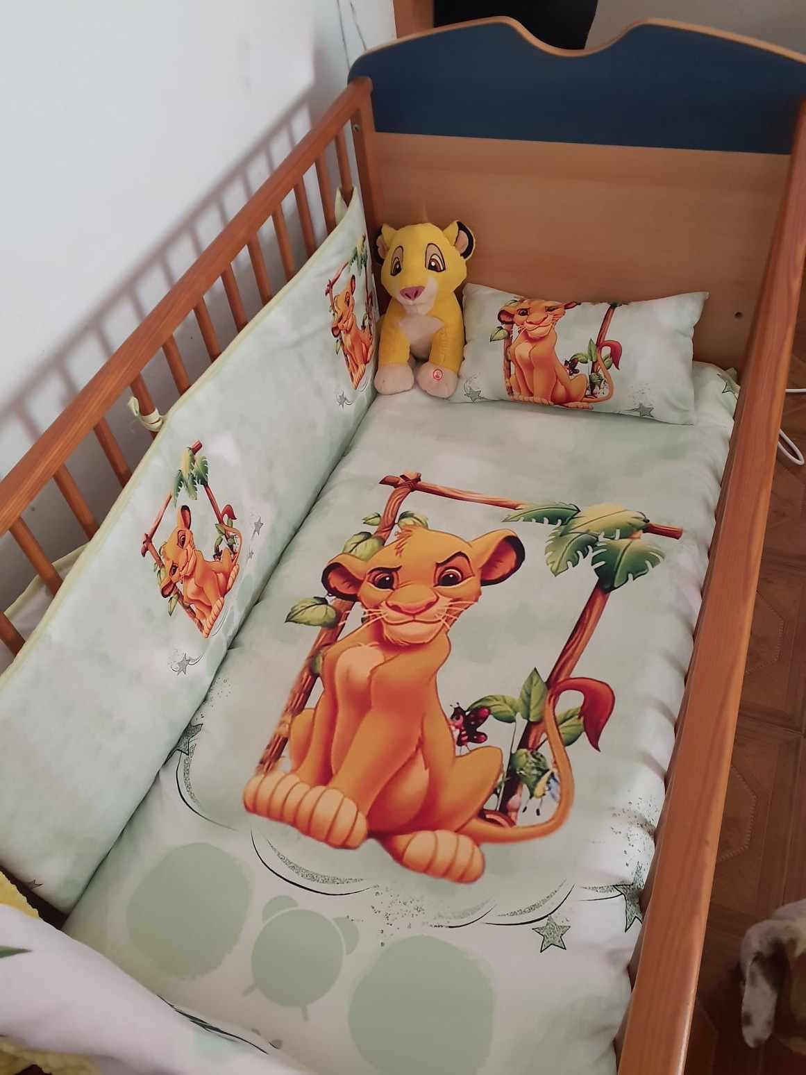 Berço de madeira com roupa de cama infantil do Rei Leão e peluche de leão amarelo