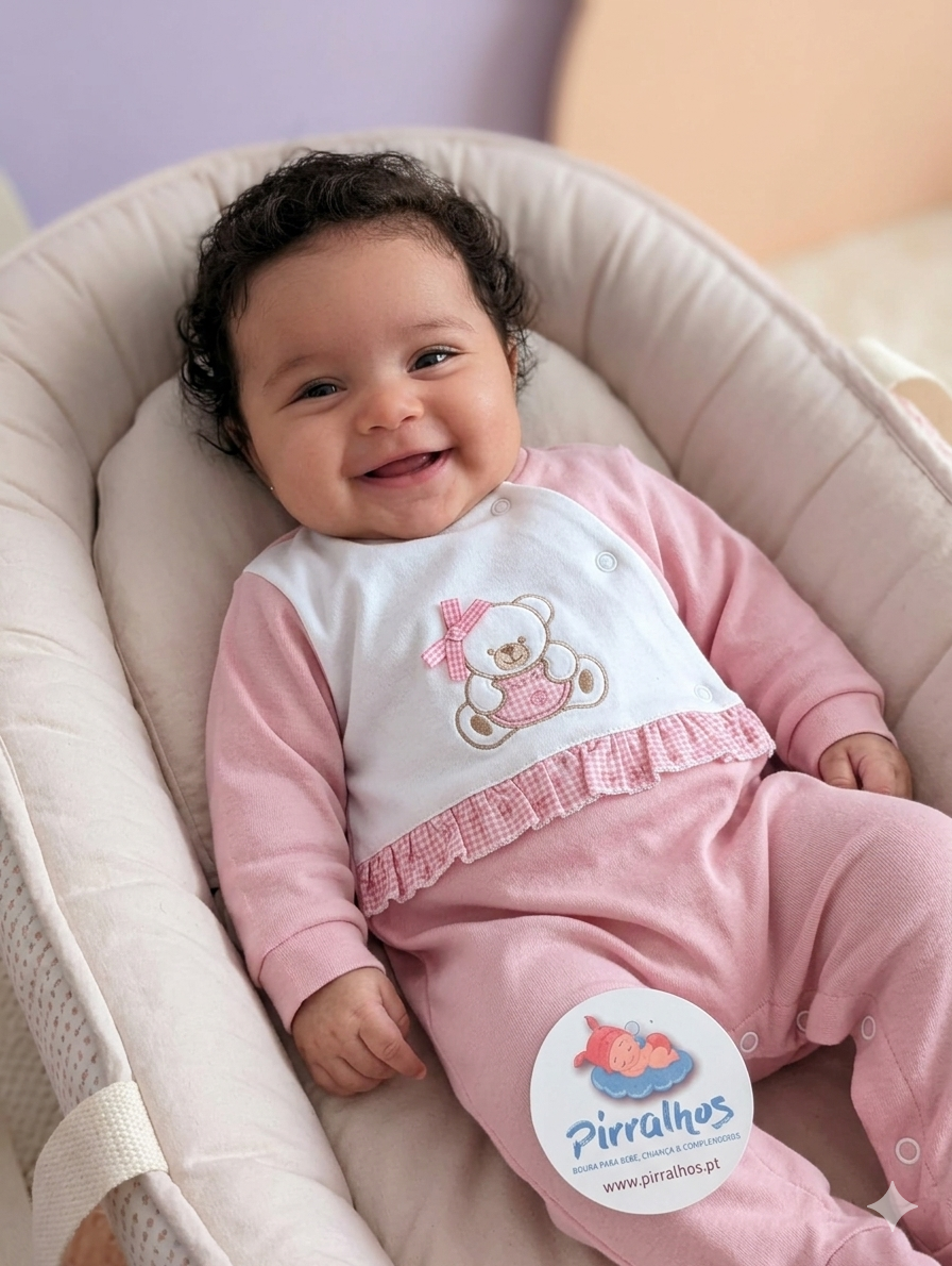 Bebé de roupa rosa e branca com ursinho bordado sentado numa almofada acolchoada bege claro, com etiqueta da marca Pirralhos.