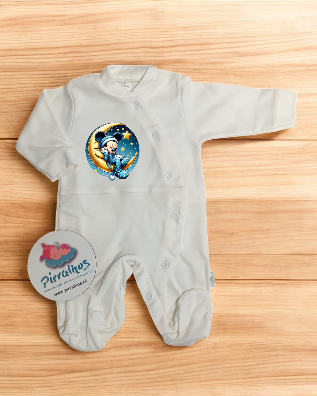 Macacão branco para bebé com estampa do Mickey na lua e etiqueta da marca Pirralhos sobre madeira clara