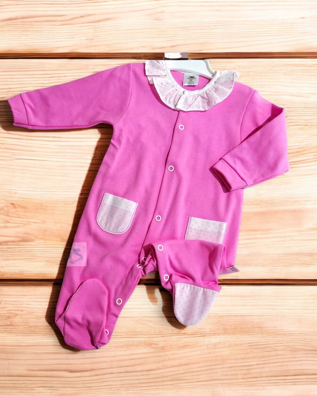 Macacão rosa de bebé com gola branca e bolsos, colocado sobre madeira clara