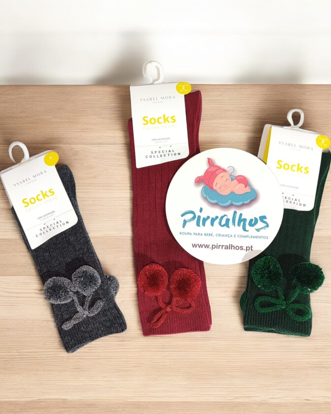 Três pares de meias coloridas de lã com pompons em superfície de madeira clara com etiquetas e cartão de marca