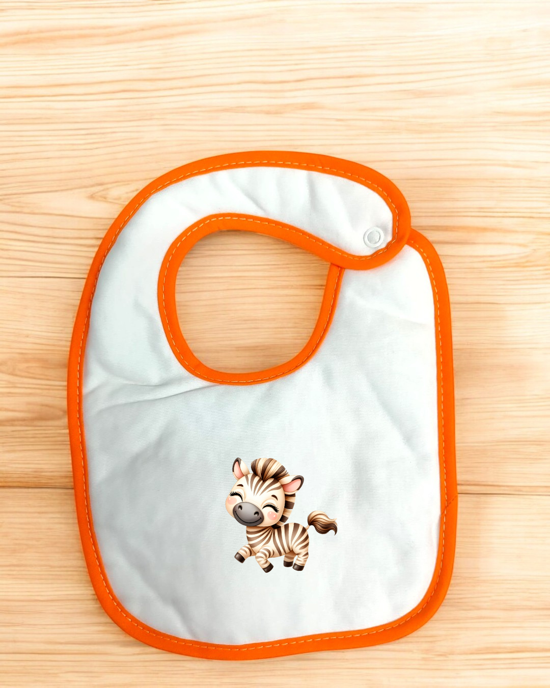 Babete branco com borda laranja e desenho de zebra, sobre madeira clara