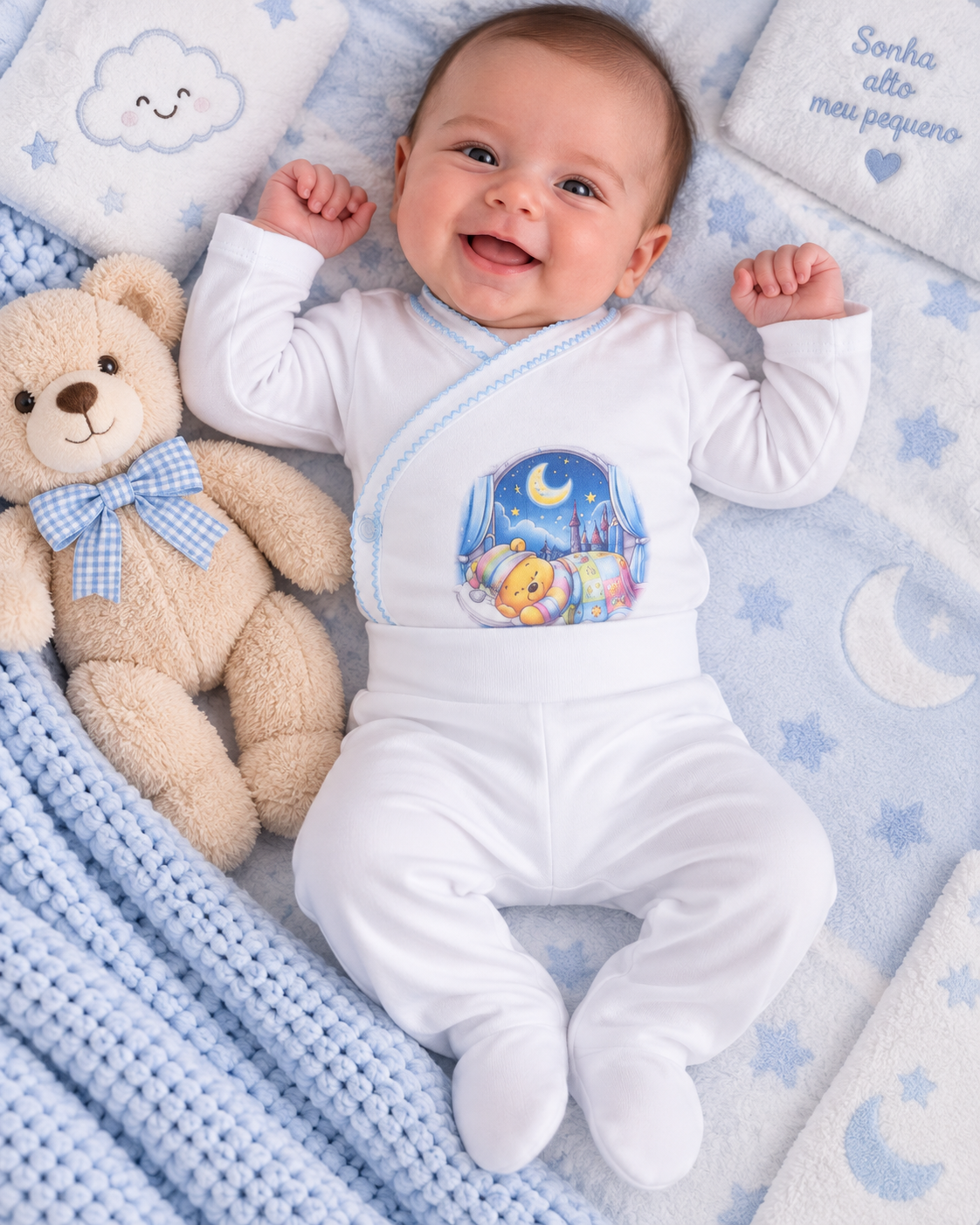 Bebé de pijama branco com estampa colorida de ursinho e lua, deitado em manta azul claro com padrão de estrelas e nuvens ao lado de urso de peluche