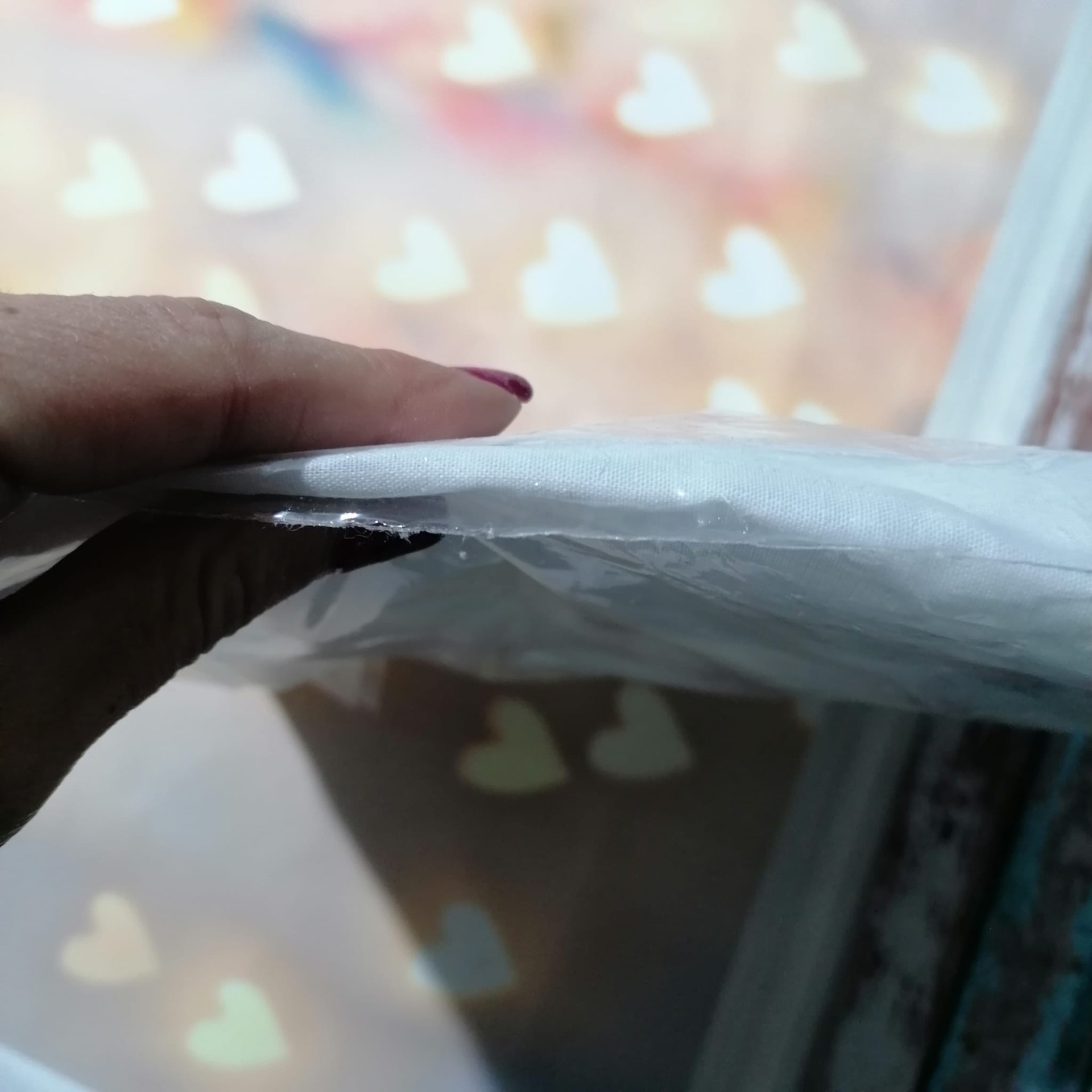 Mão a segurar embalagem plástica com objeto branco e fino, fundo com corações brancos desfocados