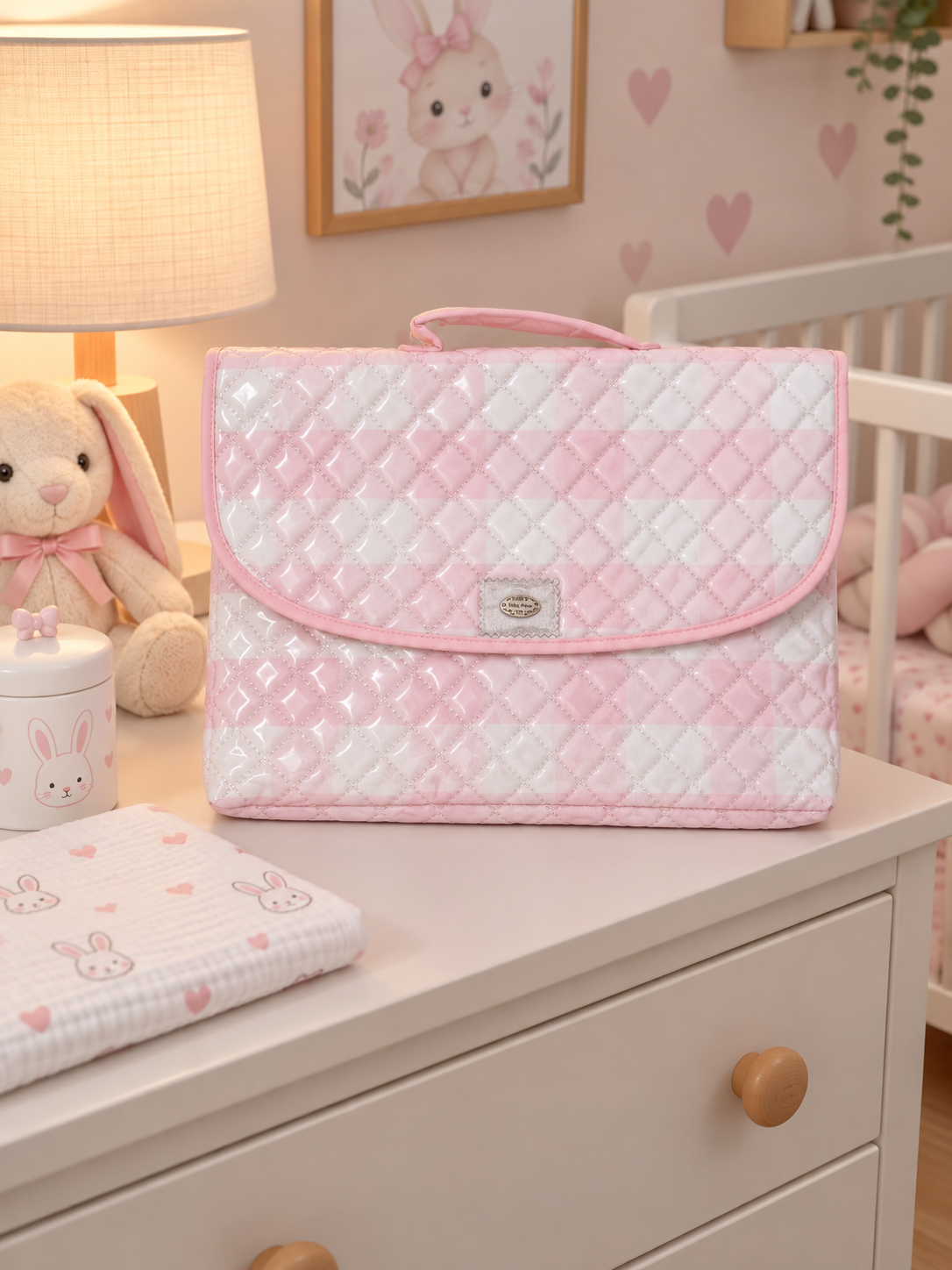 Bolsa de maternidade rosa e branca acolchoada sobre cómoda em ambiente de quarto de bebé.