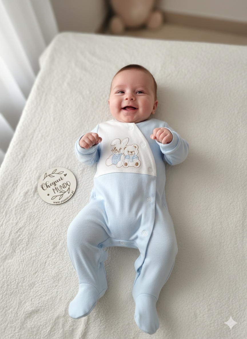 Bebé com macacão azul claro e branco com bordado de coelho e urso deitado em manta branca com placa redonda ao lado