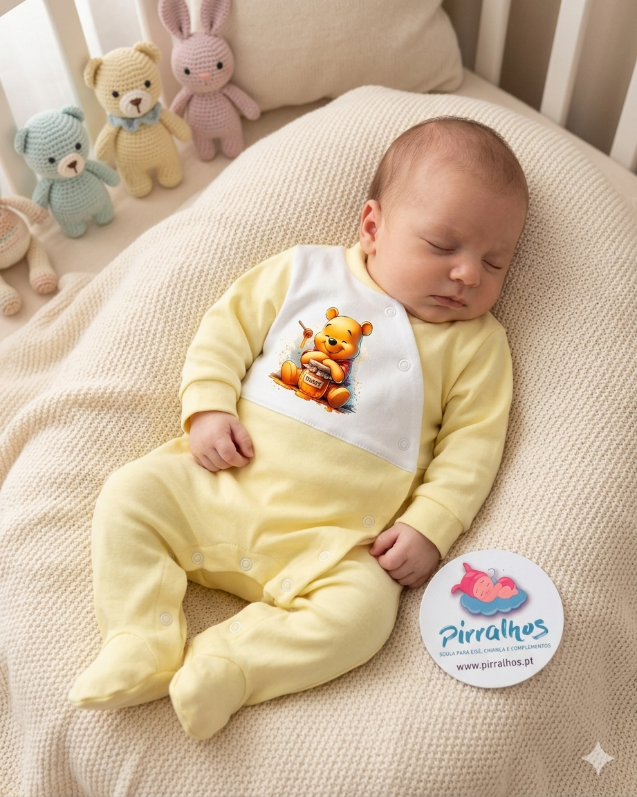 Bebé dorme com macacão amarelo com estampa de ursinho no mel, almofada bege de malha e cartão promocional ao lado
