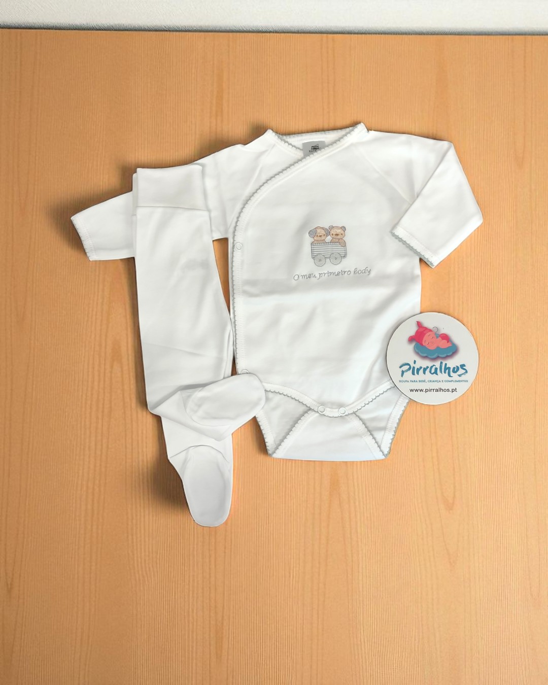 Conjunto de roupa de bebé branco com body e calças, com desenho de ursos e texto, visto numa superfície de madeira clara