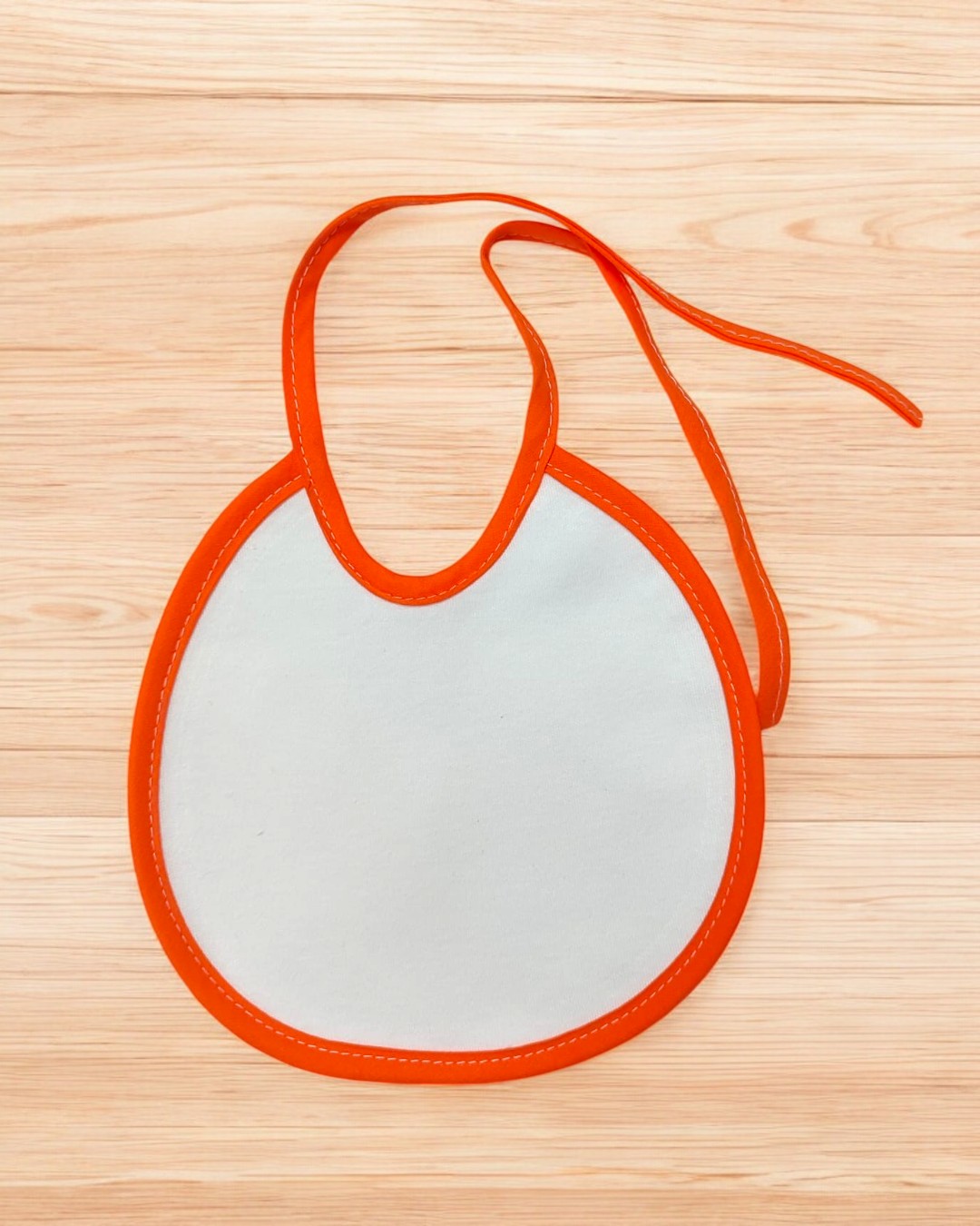 Babete infantil branco com borda laranja sobre madeira clara