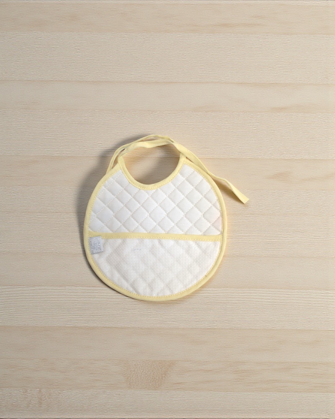 Babete de bebé acolchoado branco com bordas amarelas em superfície de madeira clara