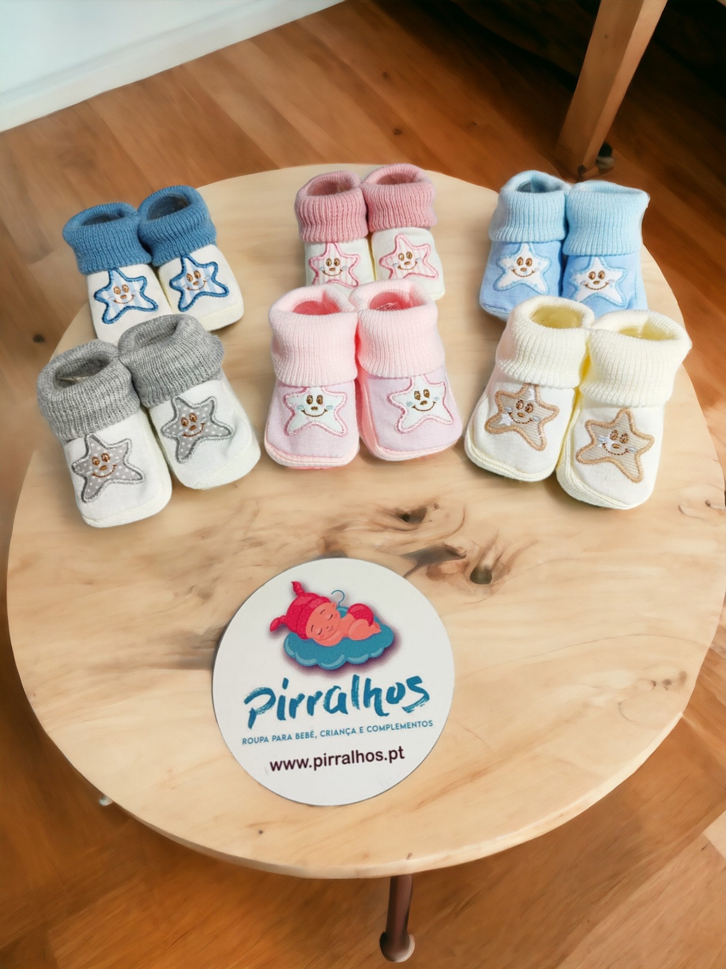 Cinco pares de meias de bebé coloridas com estrelas sorridentes, em cima de uma mesa de madeira com logótipo de marca.