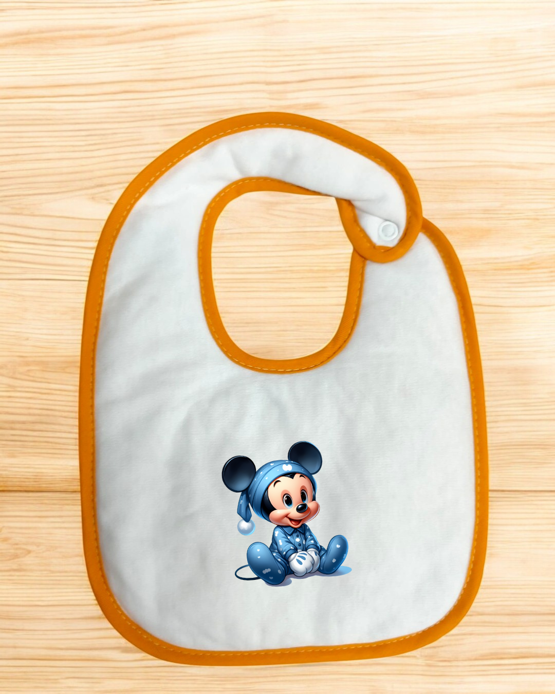 Babete branco com borda laranja e imagem de Mickey Mouse vestido com pijama azul
