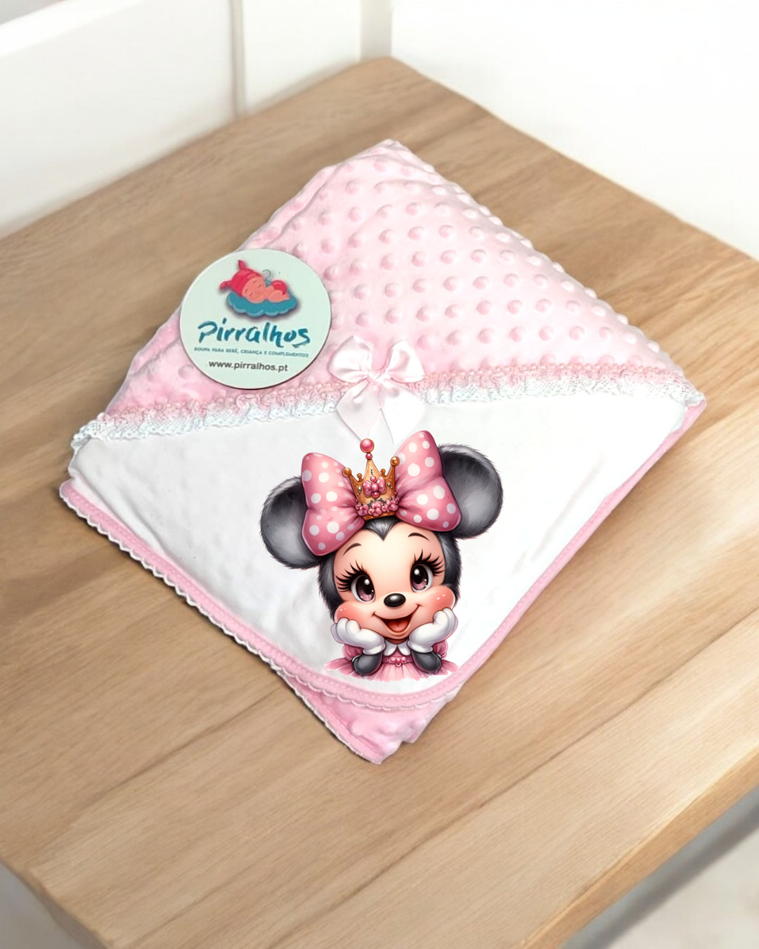 Fralda branca e rosa com imagem de rato com coroa e laço rosa, sobre mesa de madeira